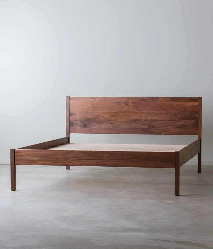 a wooden bed frame sitting on top of a cement floor next to a white wall