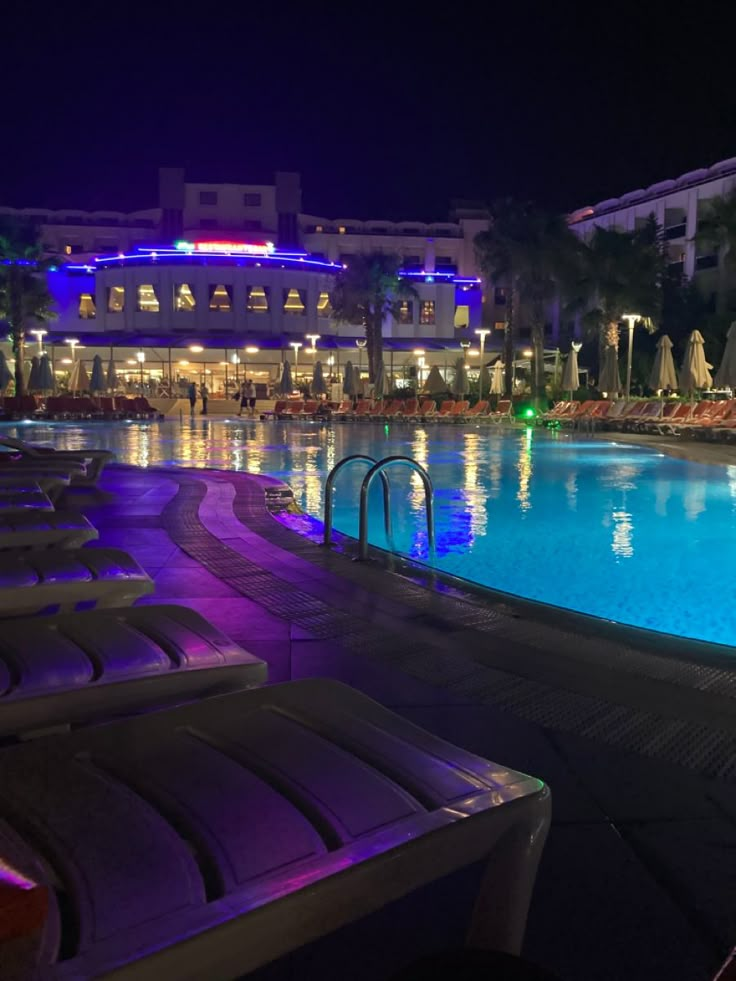 an empty swimming pool at night with lounge chairs