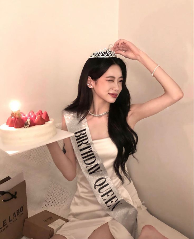 a woman sitting on a bed with a cake in front of her and wearing a tiara