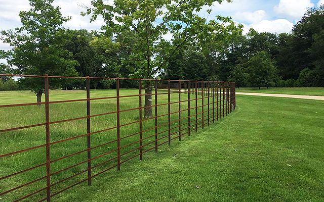 a long metal fence in the middle of a grassy field