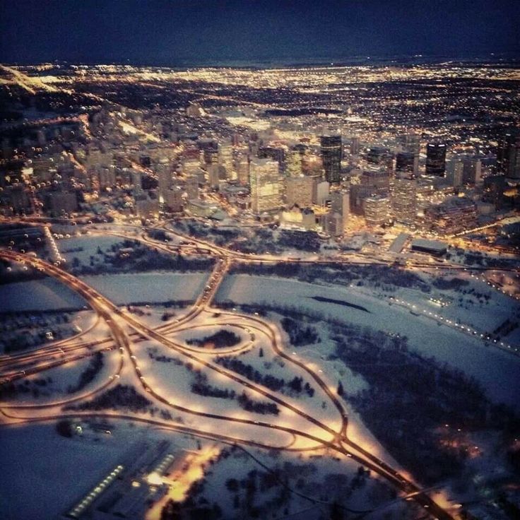 an aerial view of a city at night with lights on and snow covered ground in the foreground