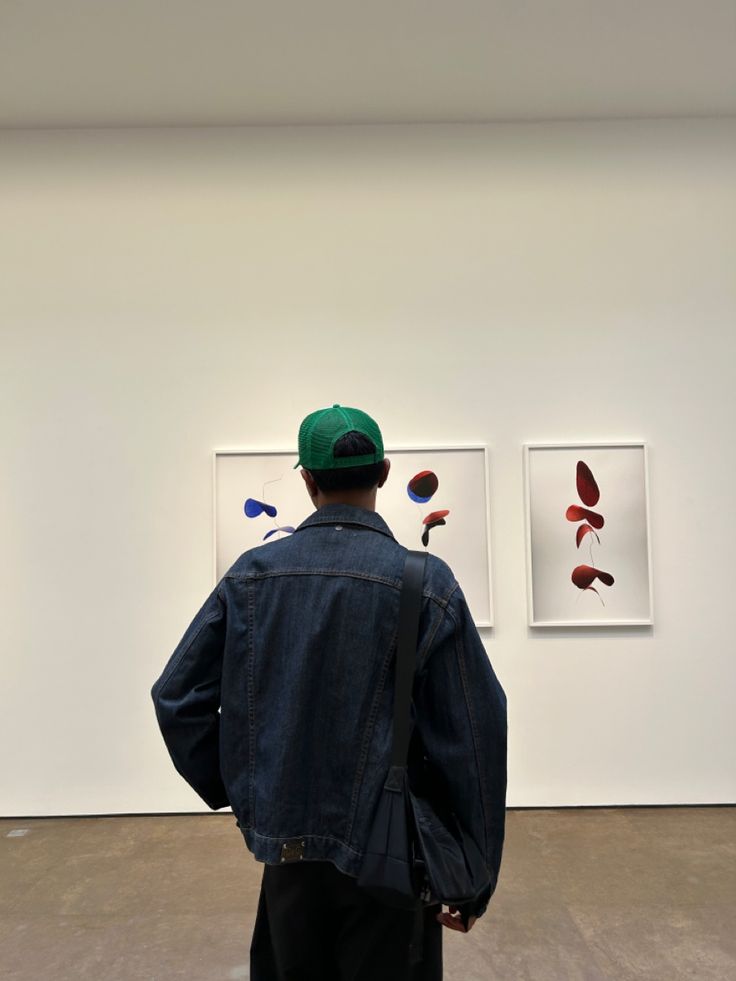 a man standing in front of two paintings on the wall and looking at each other