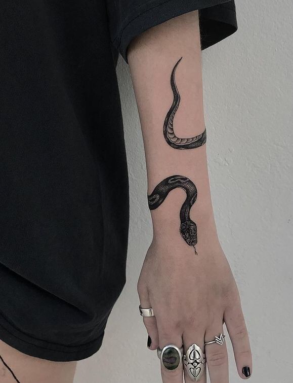 a woman's hand with a snake tattoo on her left arm and two rings around her wrist