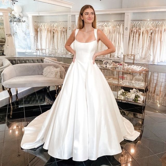 a woman standing in front of a mirror wearing a white wedding dress and looking at the camera