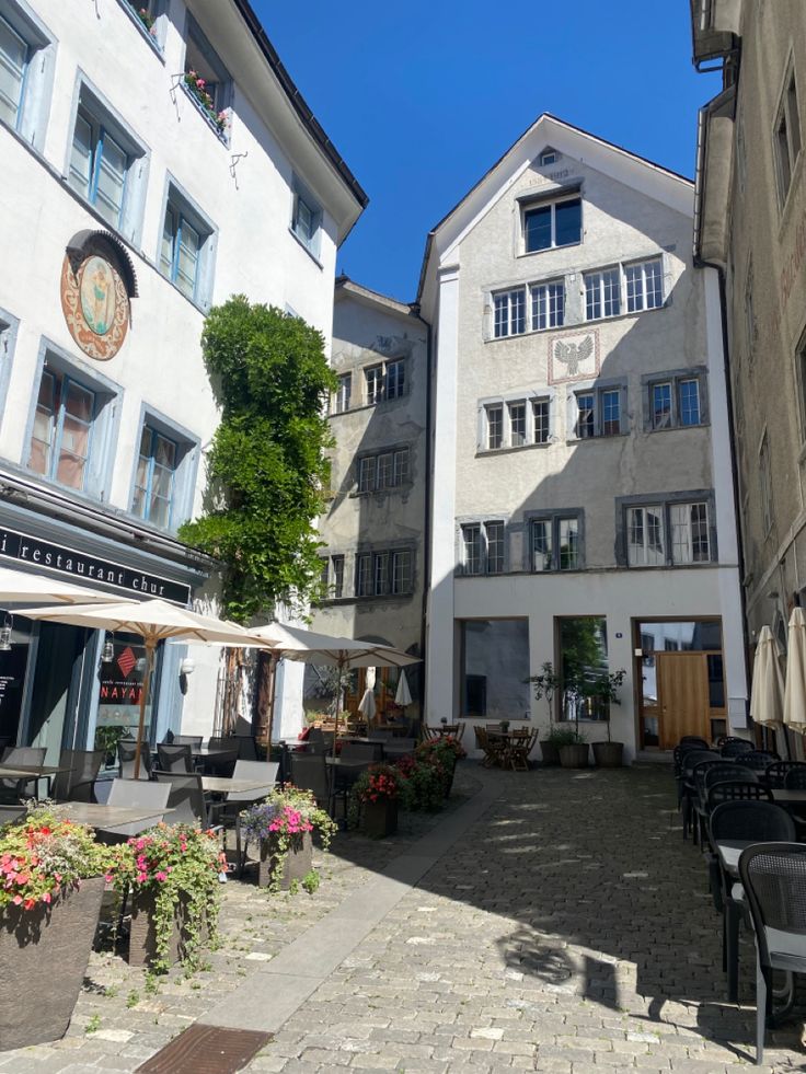 there are many tables and chairs in the courtyard outside of this building with umbrellas