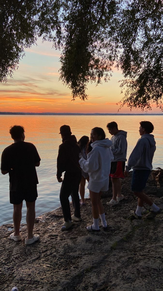 a group of people standing on top of a beach next to the ocean at sunset