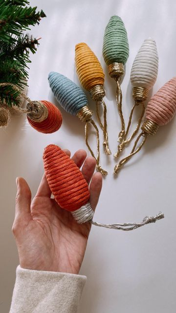 a hand is holding an ornament in front of some christmas tree ornaments on a white surface