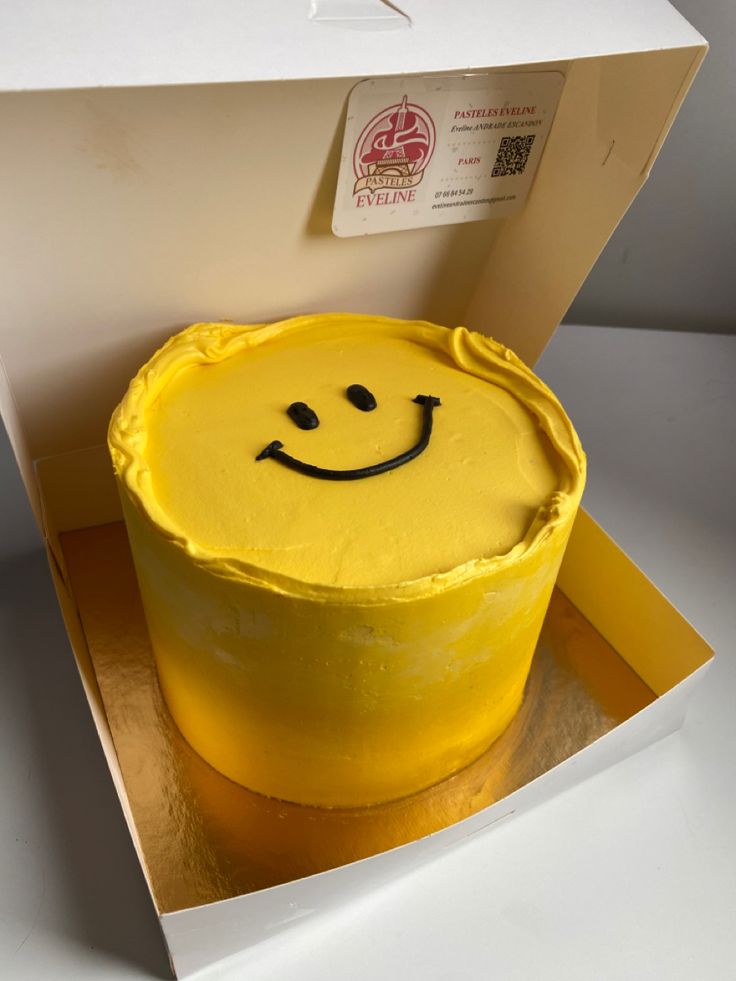 a yellow cake with a smiley face on it in a cardboard box, ready to be eaten