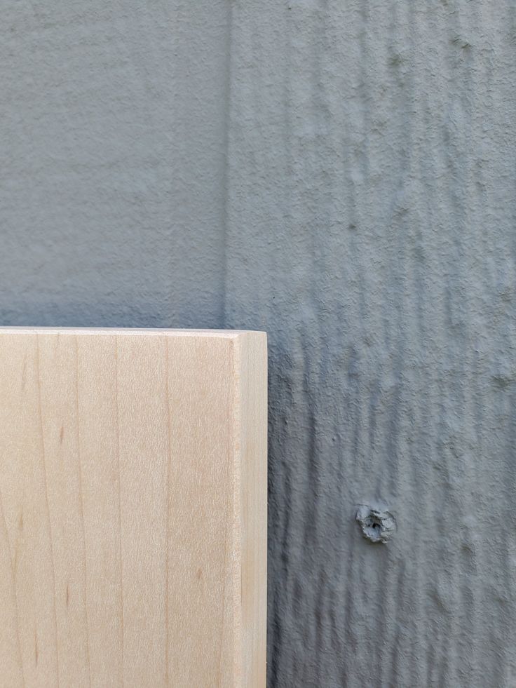 a small bird perched on top of a wooden box next to a gray and grey wall