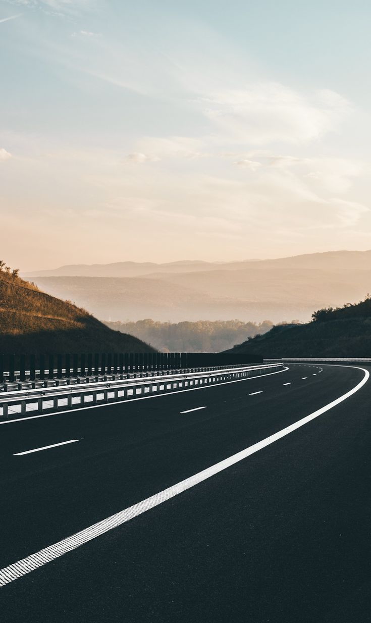 an empty highway with mountains in the background at sunset or sunrise, as seen from above