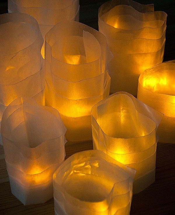 many lit candles sitting on top of a wooden table covered in plastic cups and covers