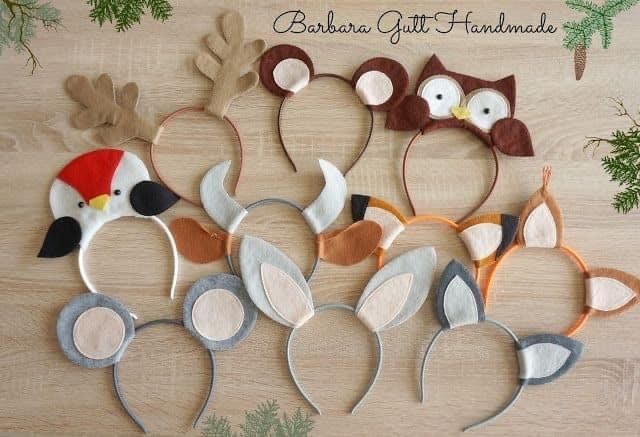 five different animal headbands on a wooden surface with pine branches in the background