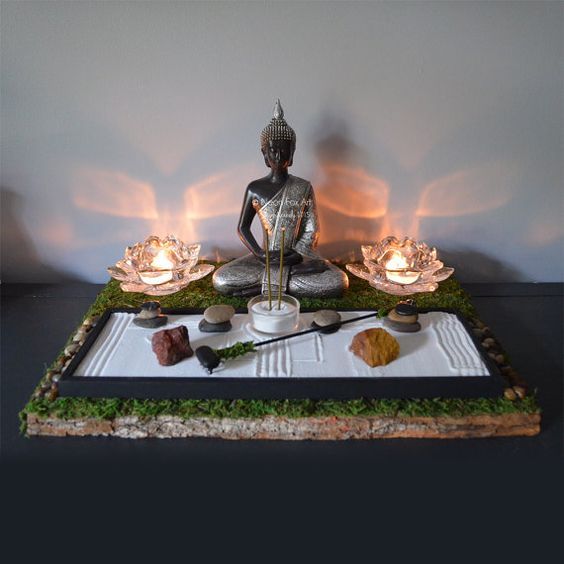 a buddha statue sitting on top of a tray filled with rocks and other items next to a lit candle