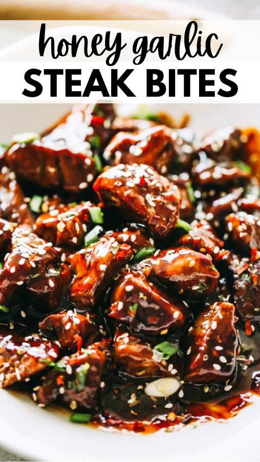 honey garlic steak bites in a white bowl with sesame seeds and green onions on the side