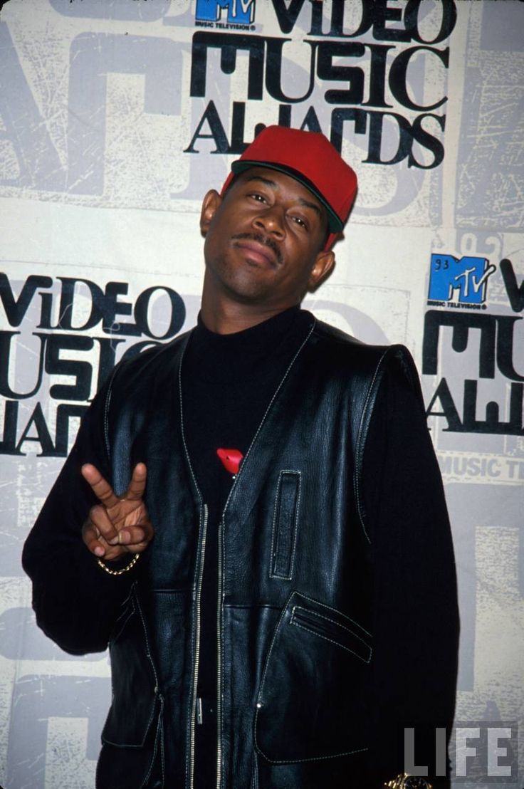 a man wearing a red hat and black jacket standing in front of a white wall