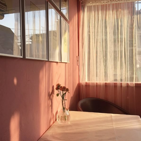 a vase with flowers sitting on top of a table next to a window in a pink room