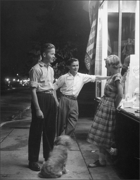 an old black and white photo of two men and a woman standing on the sidewalk