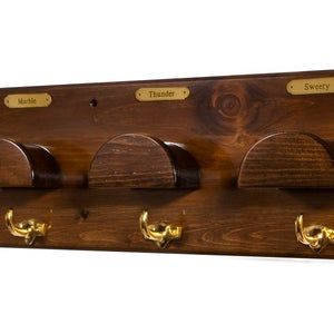 a wooden coat rack with four hooks and three coats hanging on the wall, along with brass knobs