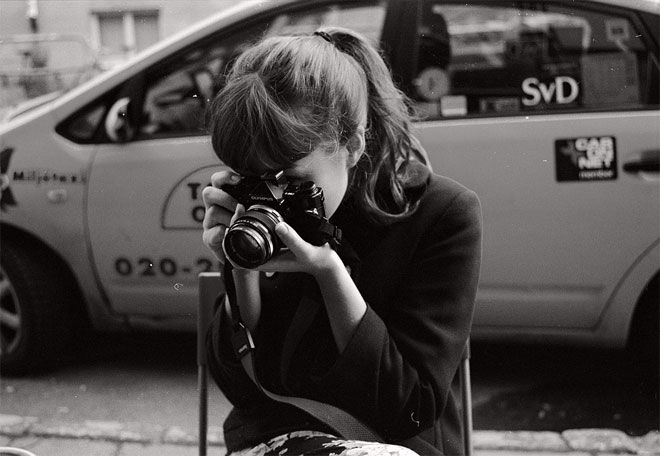 a woman sitting on a chair taking a photo with her camera in front of a car