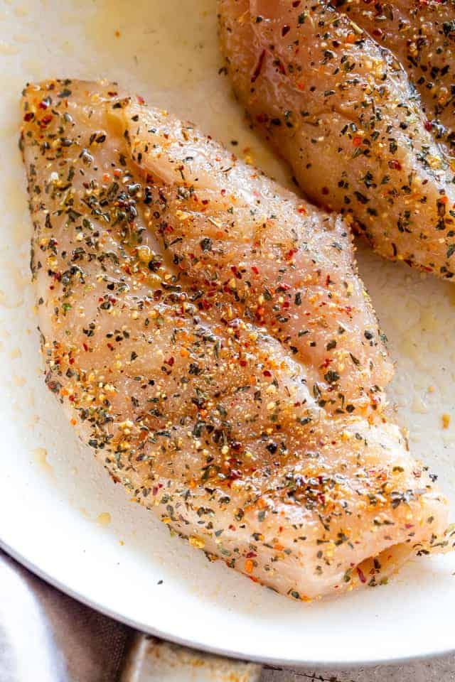 two pieces of chicken on a white plate with seasoning sprinkled around them