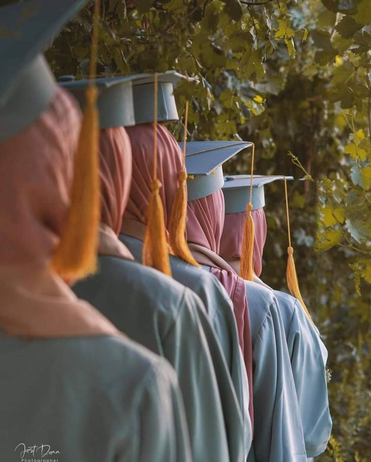 a row of graduation gowns hanging on the side of a tree with orange tassels