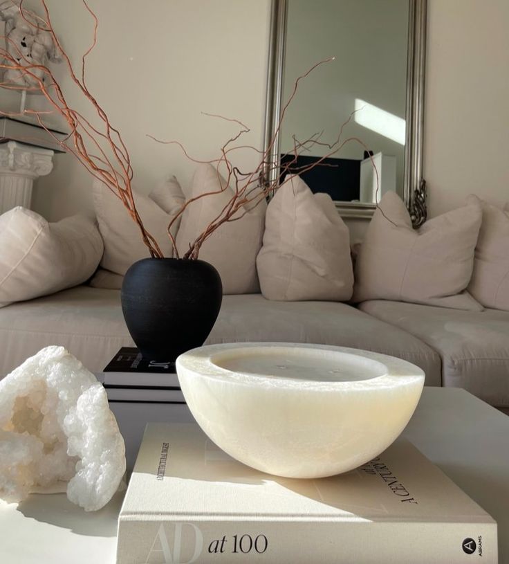 a white couch sitting next to a black bowl on top of a table in front of a mirror