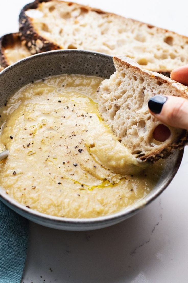 a person holding a piece of bread over a bowl of soup