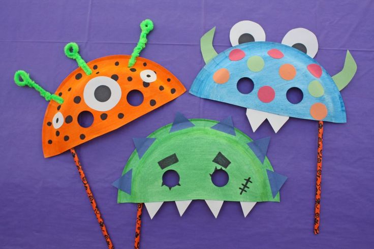 three paper monster masks on purple background with green and orange one has eyes, the other has teeth