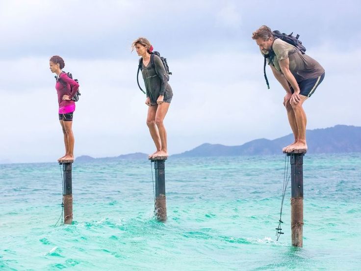 three people are standing on poles in the middle of the ocean and one person is wearing a backpack