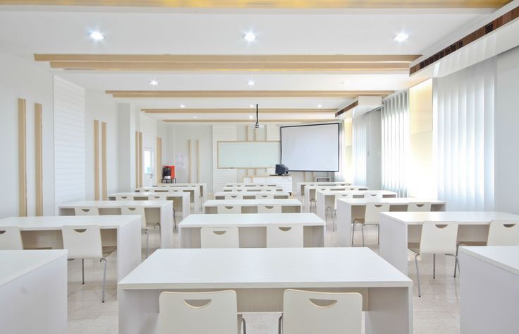 an empty classroom with white desks and chairs in front of a projector screen