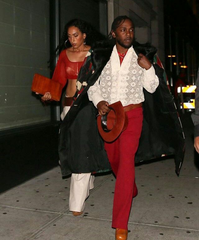 two people walking down the street at night with one person wearing a hat and another carrying a purse