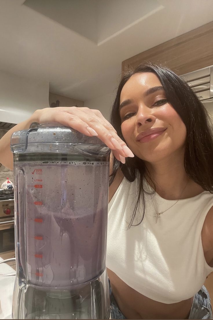 a woman standing in front of a blender with liquid on it's side