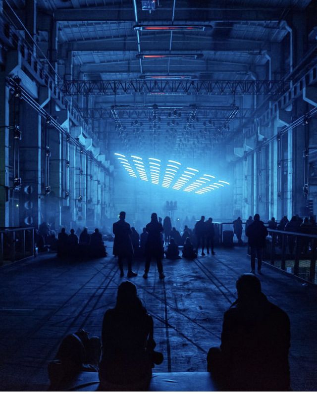 people are sitting and standing in an industrial building with blue light coming from the ceiling