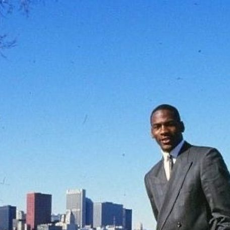 a man in a suit and tie standing next to a body of water with buildings in the background