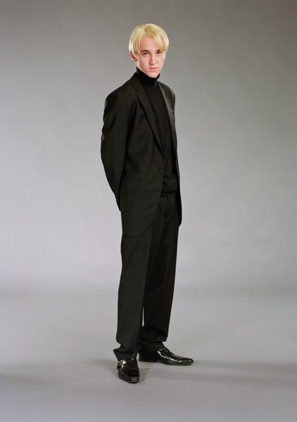 a young man in a black suit and tie posing for a photo with his hands on his hips