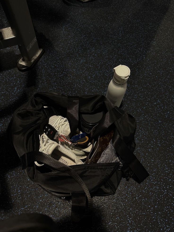 an open duffel bag sitting on the floor next to a bottle and other items