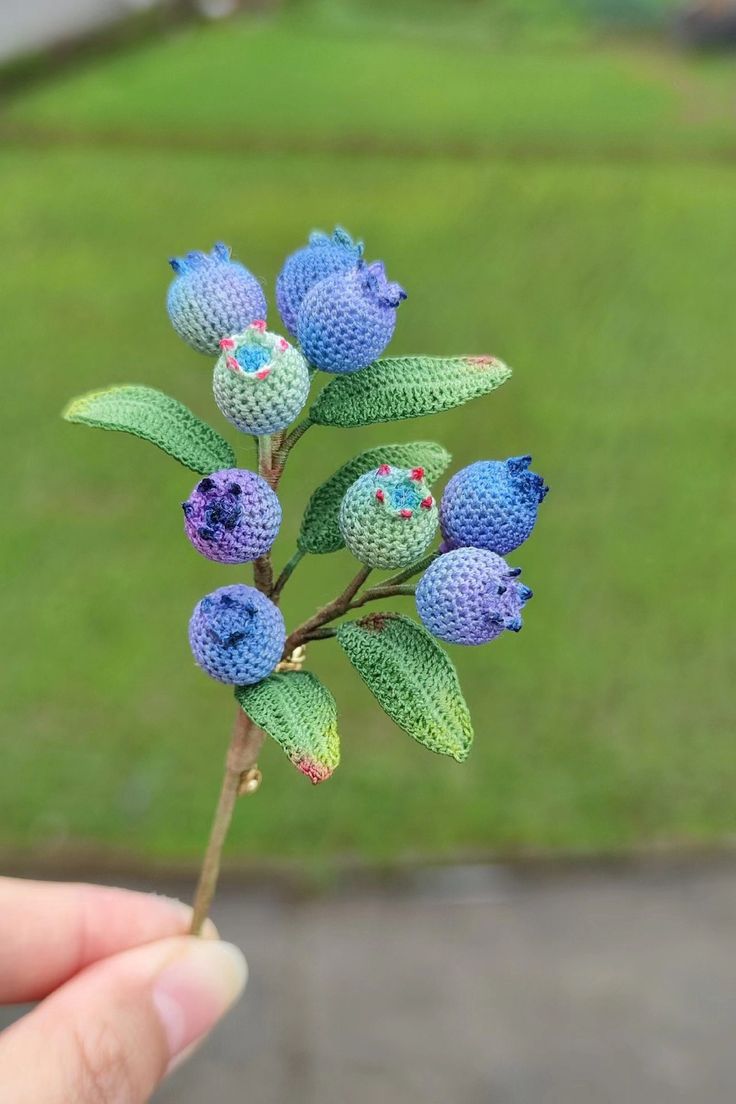 a hand holding a tiny blue flower with green leaves