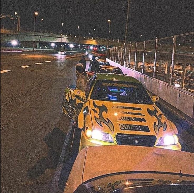 a yellow car with flames painted on it parked in front of a parking lot at night