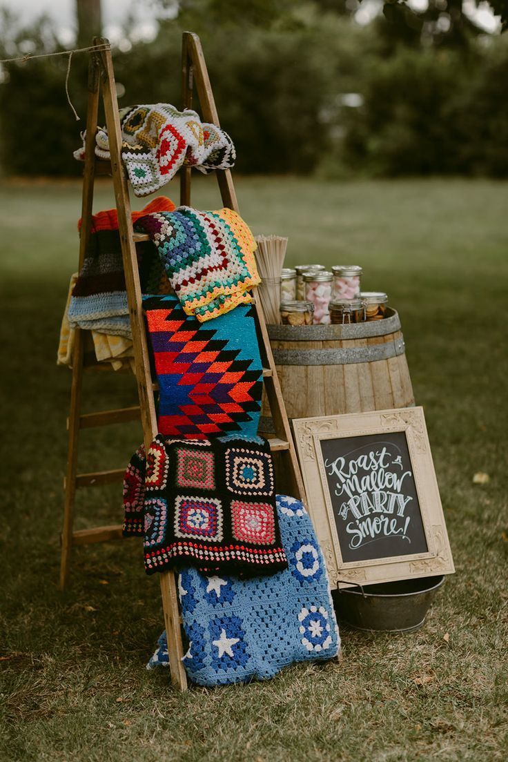 a wooden ladder holding blankets and crocheted items in the grass next to a chalkboard