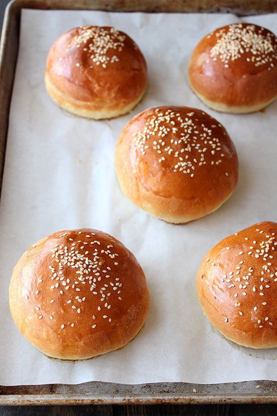 six buns with sesame seeds sit on a baking sheet