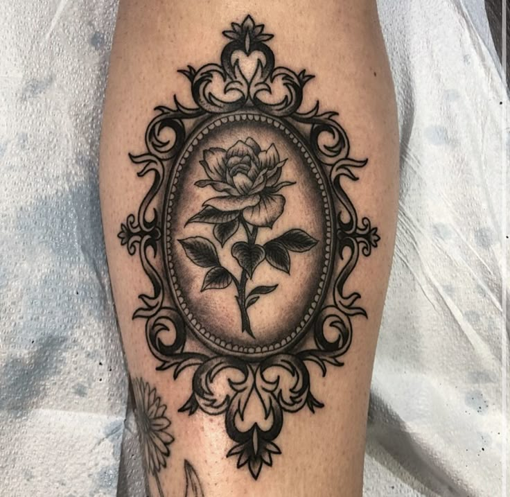 a black and white photo of a rose in a frame tattoo on the right leg