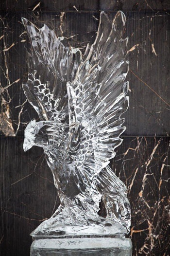 a glass sculpture of a bird on top of a marble block with black and white marble behind it