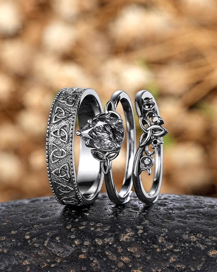 two wedding rings sitting on top of a rock next to another ring with an intricate design