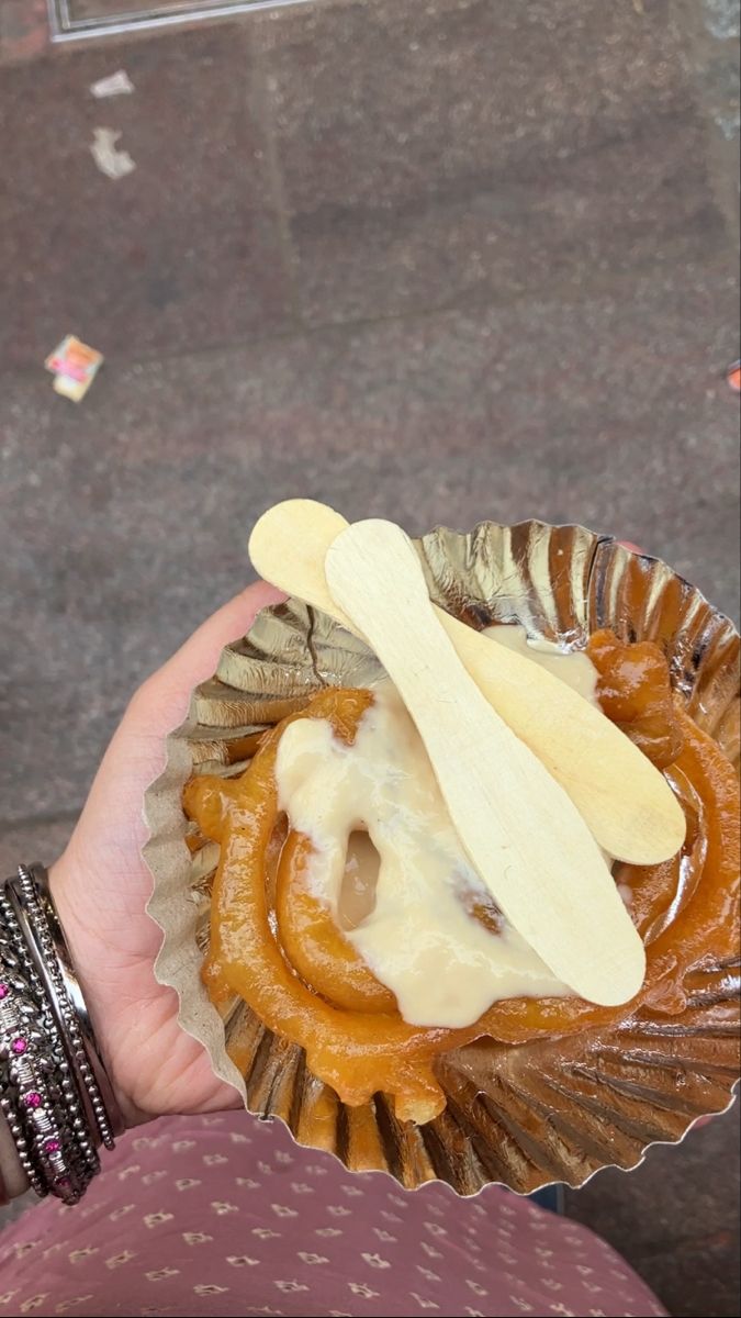 a person holding a pastry with icing and spoons in their hand on the street