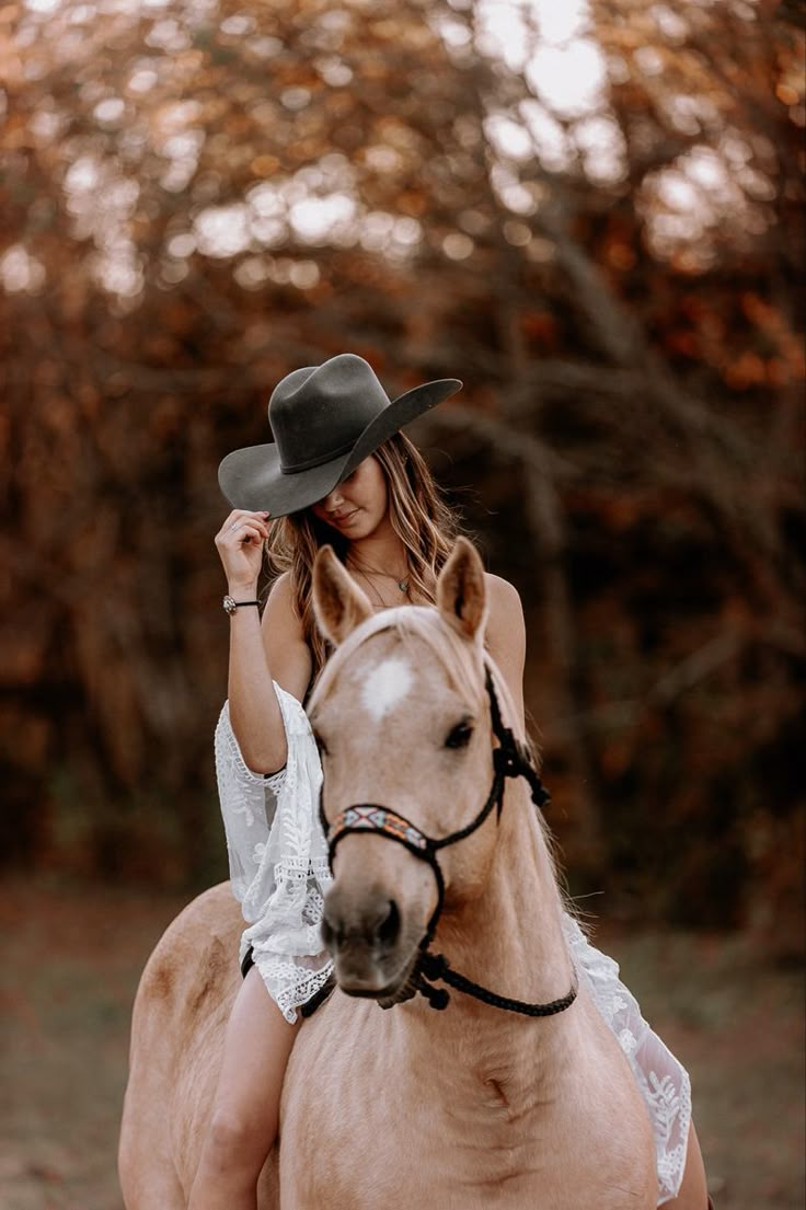 a woman sitting on top of a horse wearing a cowboy hat and white lace dress