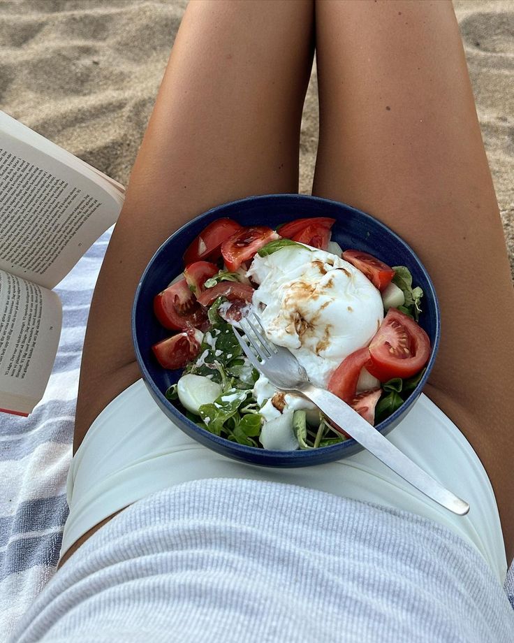 a person laying on the beach with a bowl of food in front of their legs