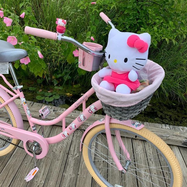 a pink hello kitty bike with a basket on the front and side, parked on a wooden deck