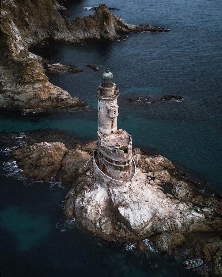 an aerial view of a lighthouse on top of a rocky outcropping next to the ocean