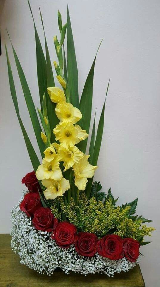 a vase filled with yellow and red flowers on top of a wooden table next to a white wall