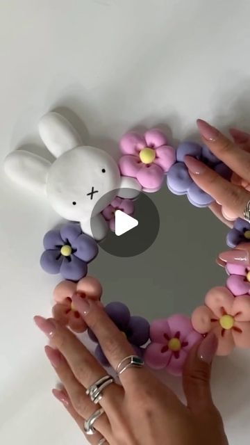 two hands are holding up some fake flowers in front of a mirror with a bunny on it